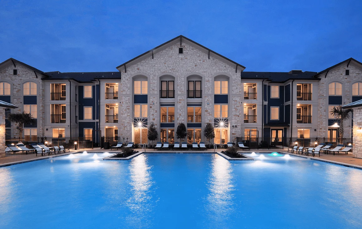 Apartment building lit at dusk beside a glowing swimming pool