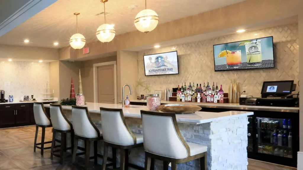 Bar counter with white stools, shelves of bottles and wall-mounted TVs
