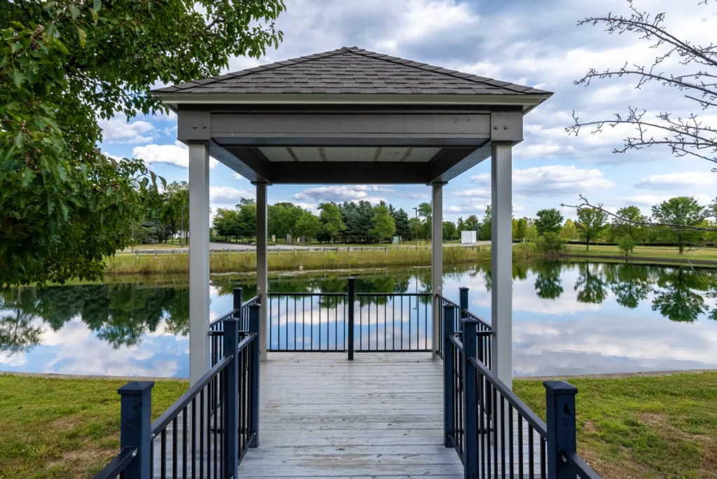 Covered gazebo on a wooden dock over a calm pond with reflections