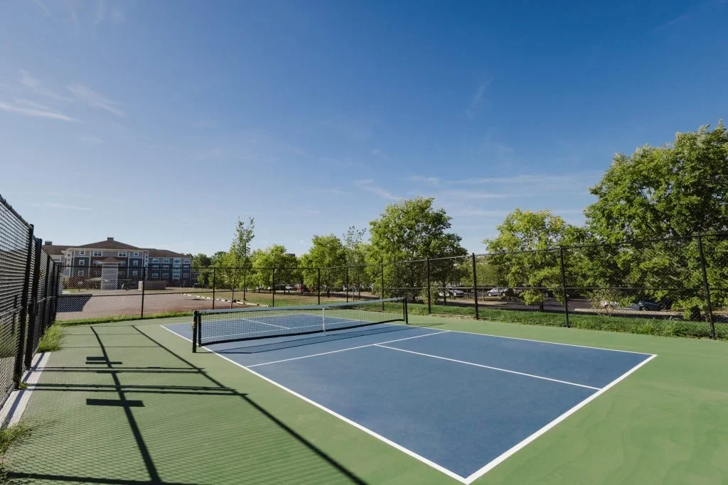 Outdoor pickleball court with blue and green surface and net, surrounded by trees under a clear sky