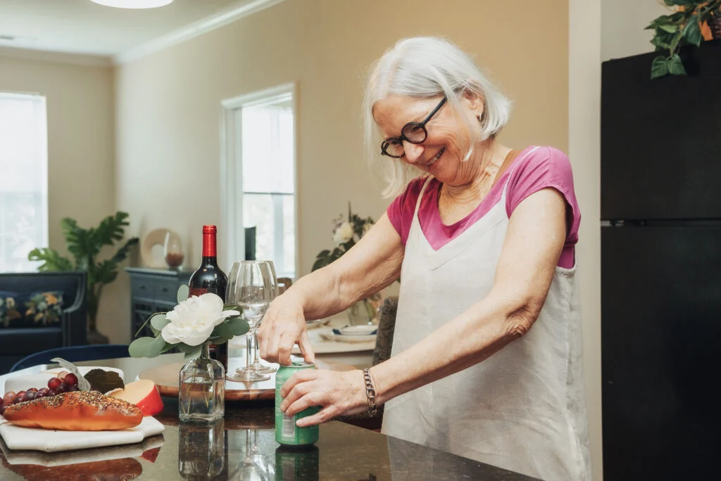 Smiling older woman in an apron and glasses preparing food at a kitchen counter