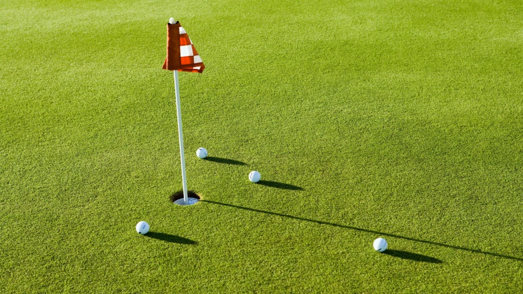 Golf ball on a putting green near a red flagstick, with additional balls scattered nearby