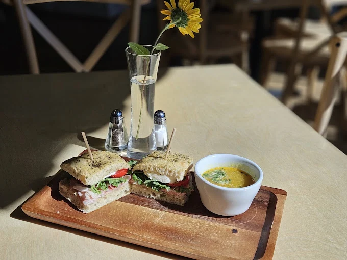 Sandwich halves and a bowl of soup on a wooden tray, with a small flower vase and salt and pepper shakers