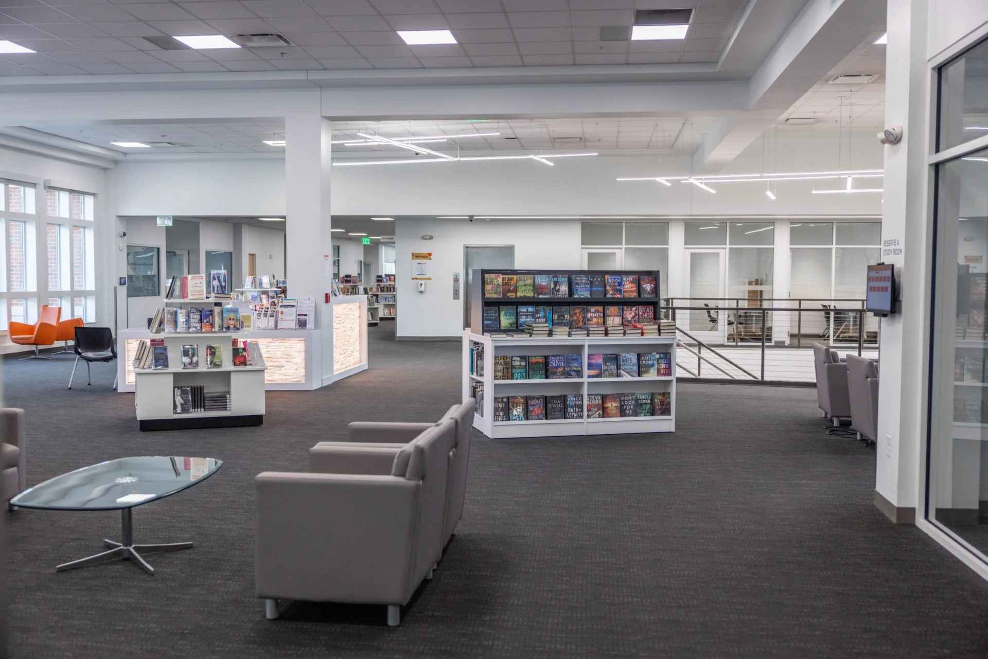 A modern library interior in Hilliard, Ohio, featuring luxury gray armchairs, a glass coffee table, bookshelves with colorful books, and bright natural light streaming through large windows—perfect for senior relaxation.