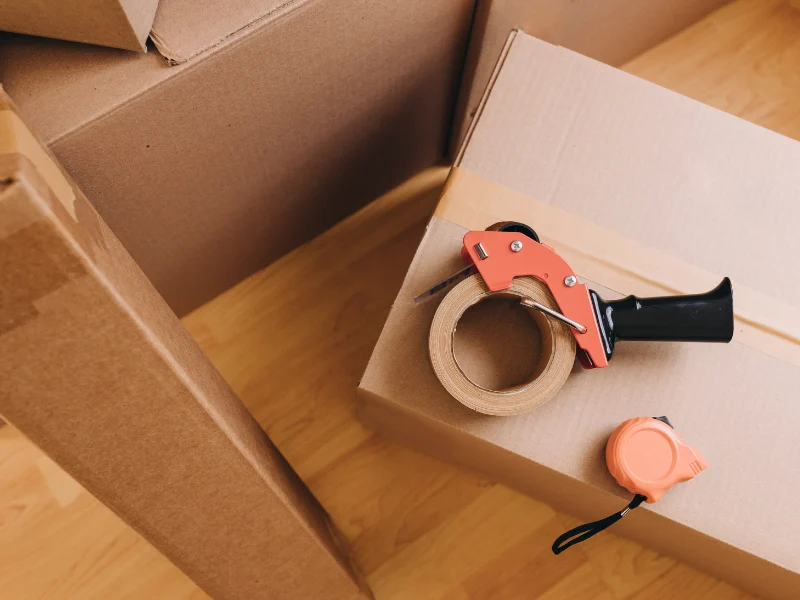 Cardboard boxes with a tape dispenser and measuring tape on a wooden floor