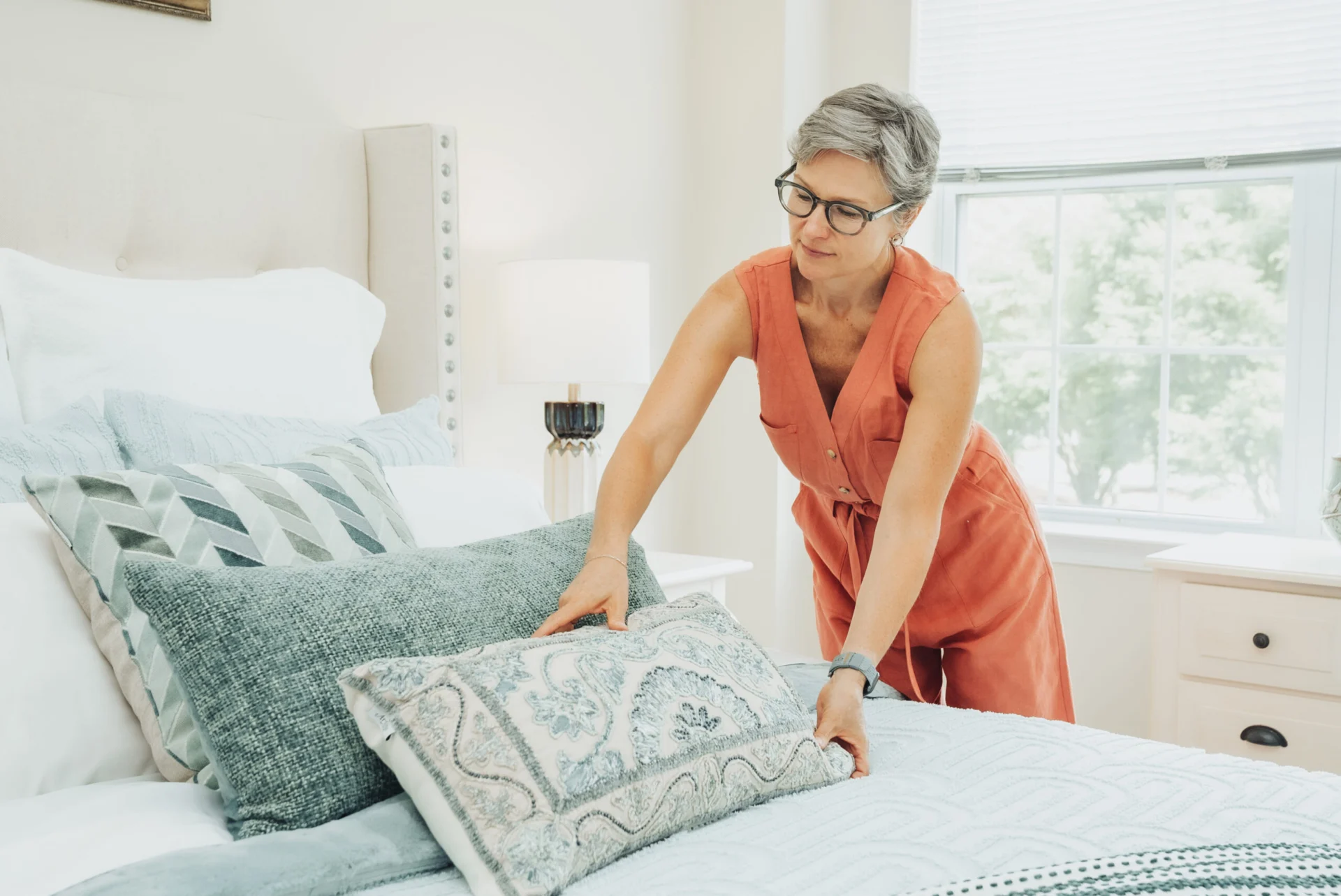 Woman arranging teal and patterned pillows on a made bed