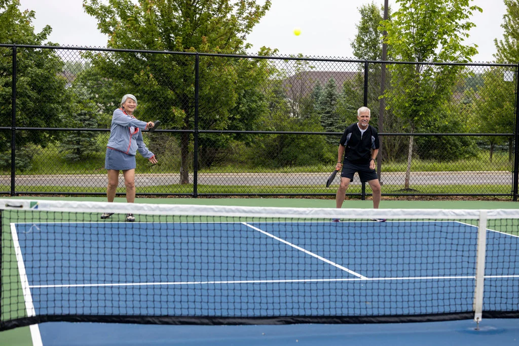 Two older adults playing a game on a blue outdoor court with a net