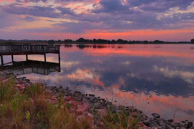 Pink and purple sunset reflected in a calm lake beside a wooden pier
