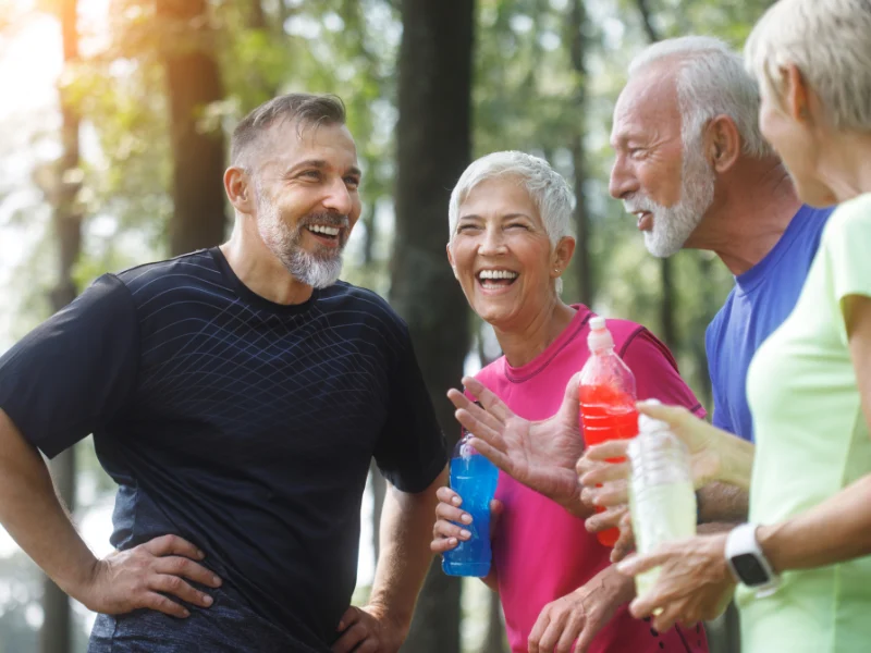 Group of older adults laughing together outdoors while holding water bottles