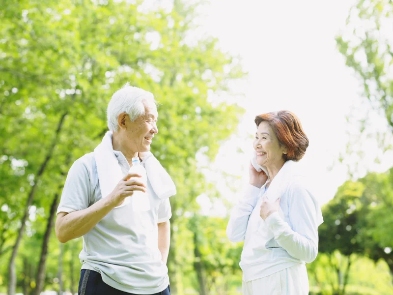 Two older adults in workout clothes chatting outdoors among trees