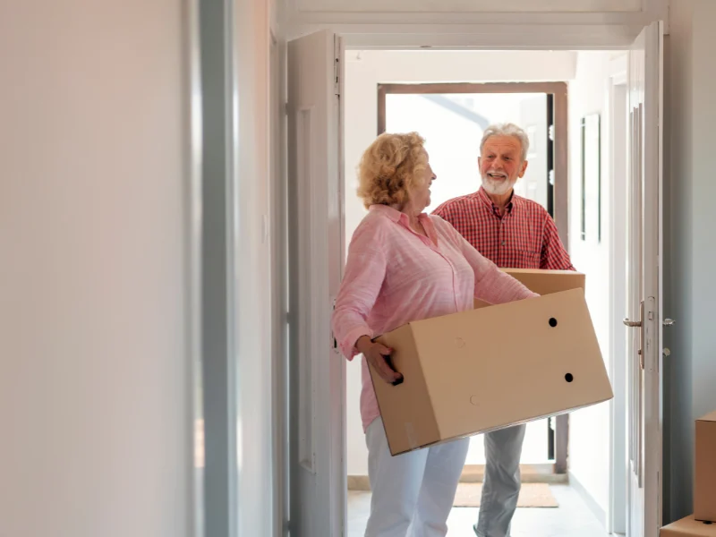 Smiling older couple carrying a cardboard box through a doorway