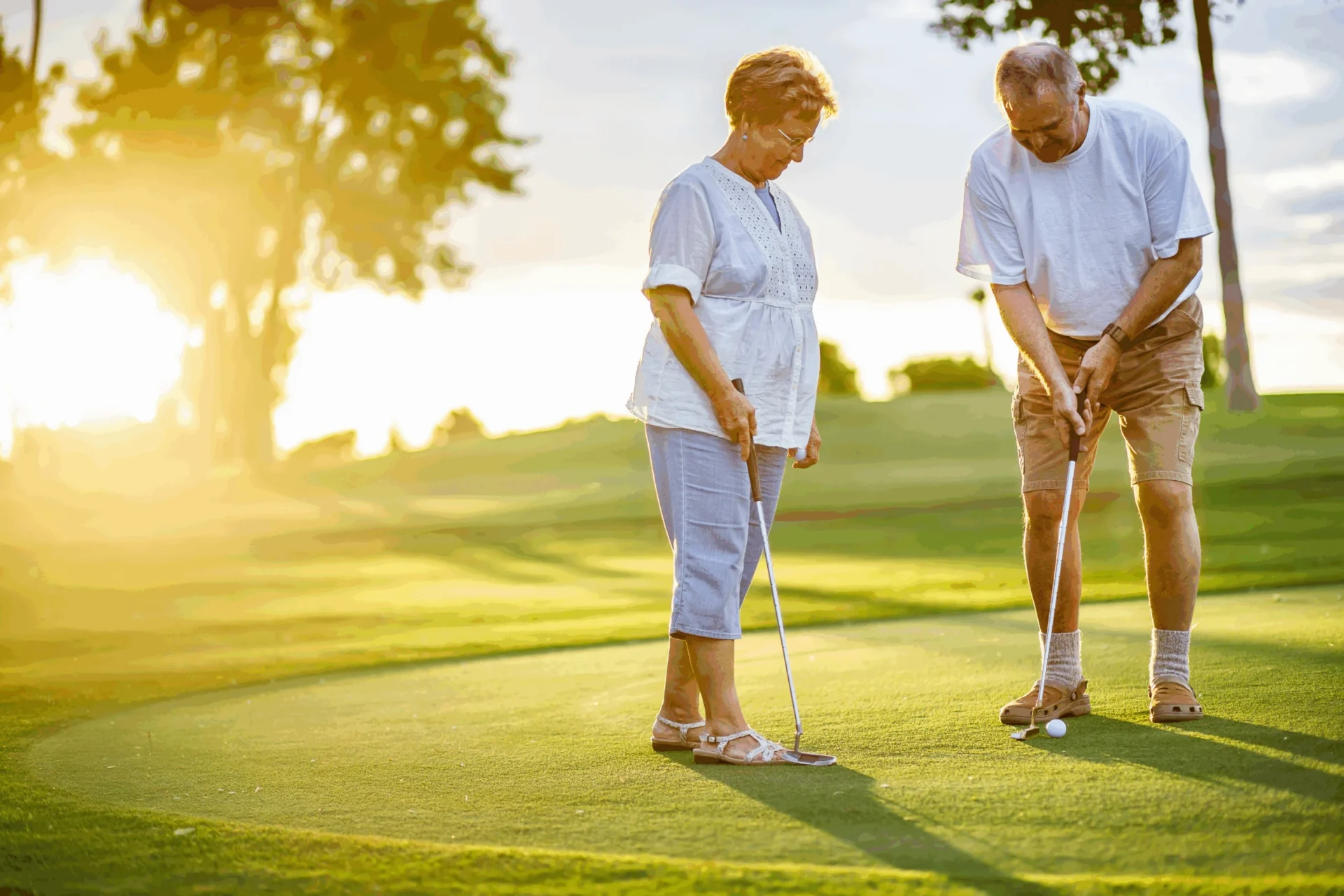 Senior couple playing golf on a putting green at sunset