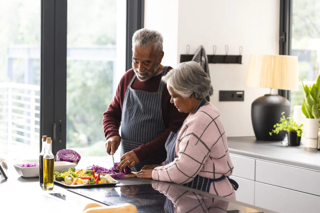 Two older adults in aprons chopping vegetables together in a bright kitchen