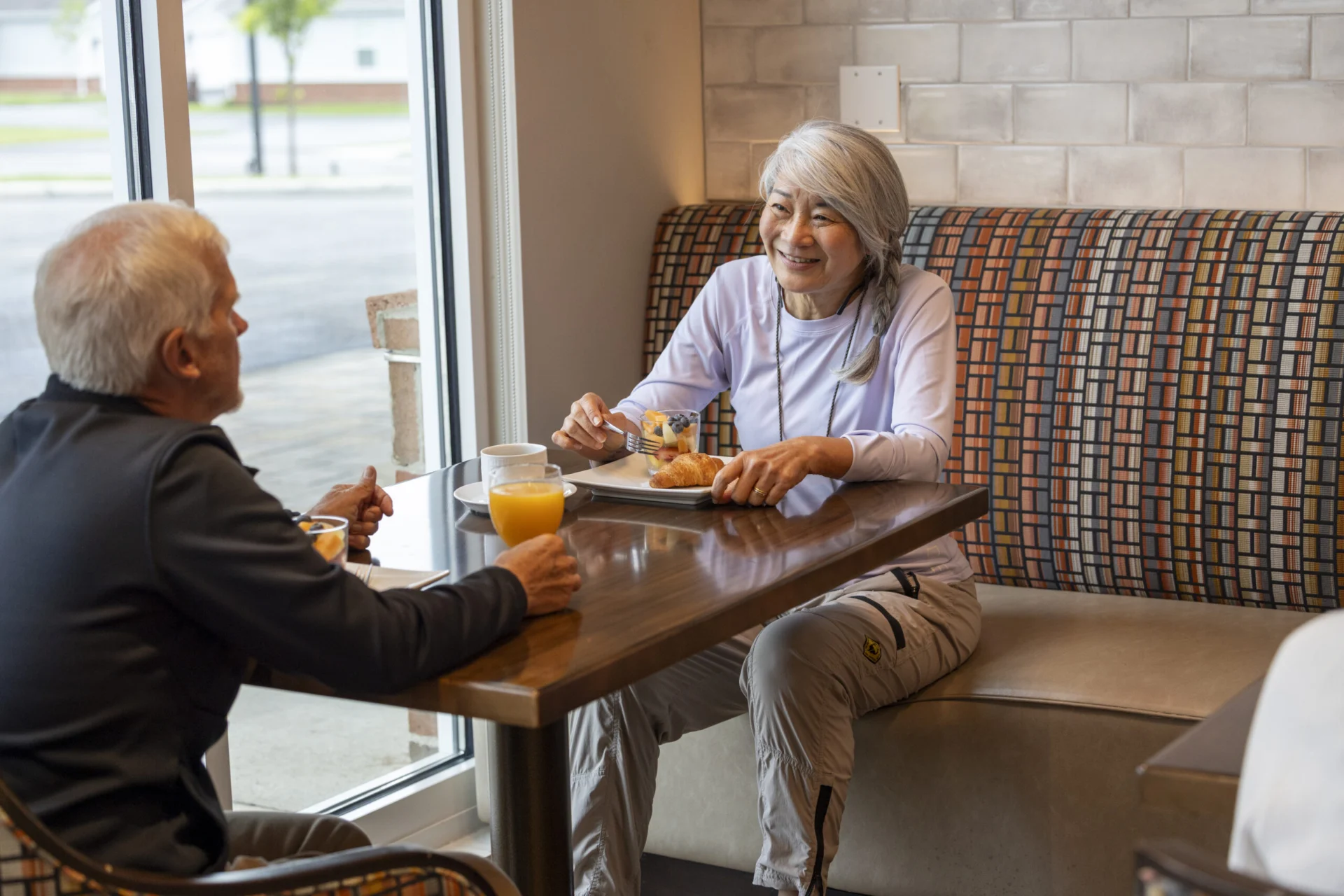 Older man and woman talking over a meal at a booth by a window