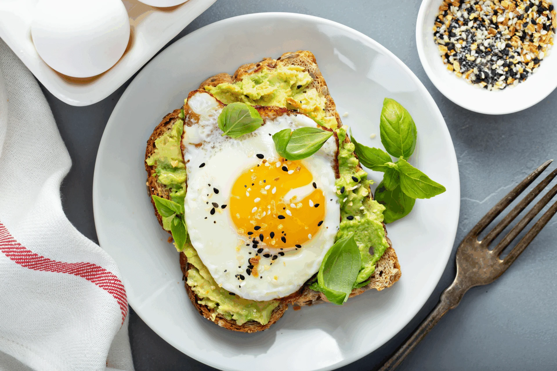 Avocado toast topped with a fried egg and basil on a white plate