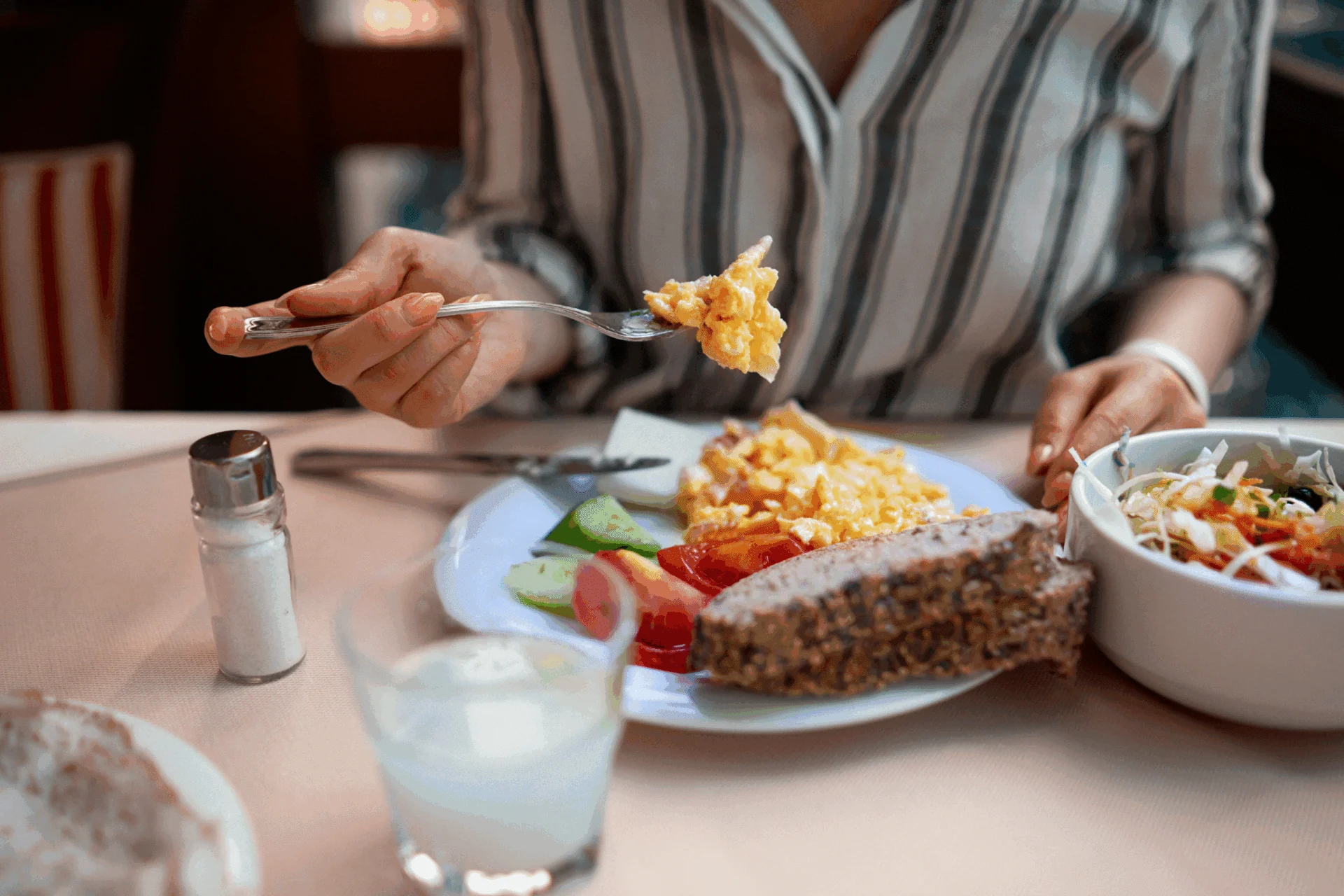 Breakfast plate of eggs, toast and salad on a table, with a person eating