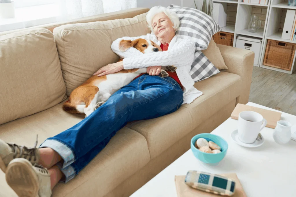 Older woman relaxing on a sofa with a small dog, with a cup of tea and a small bowl on the coffee table