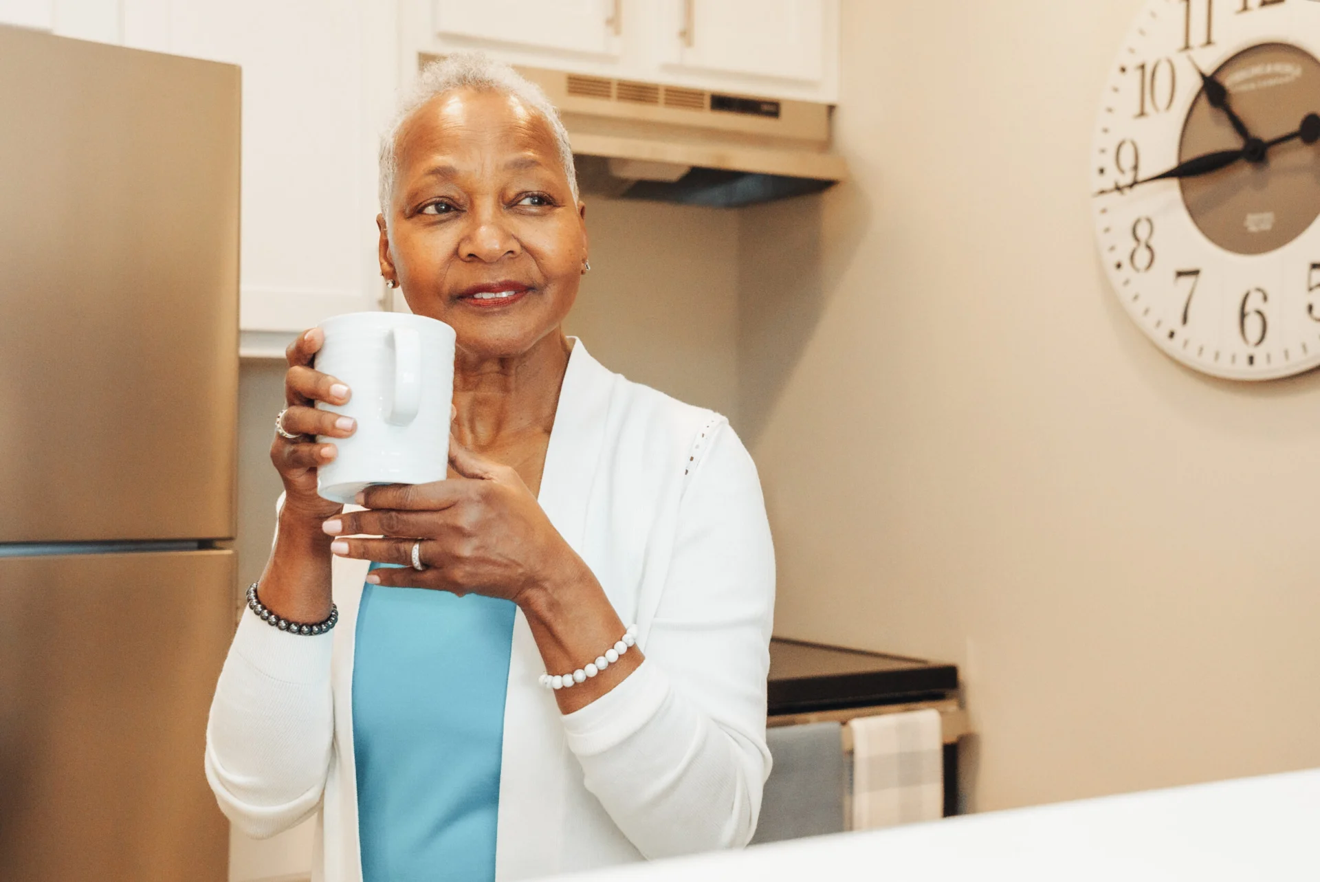 Older woman smiling and holding a white mug in a kitchen