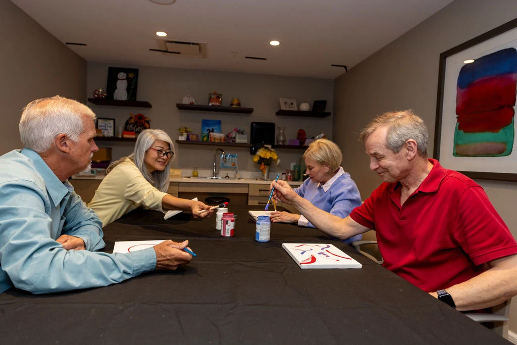 Group of older adults playing a board game around a dark table in a lounge with shelves and art