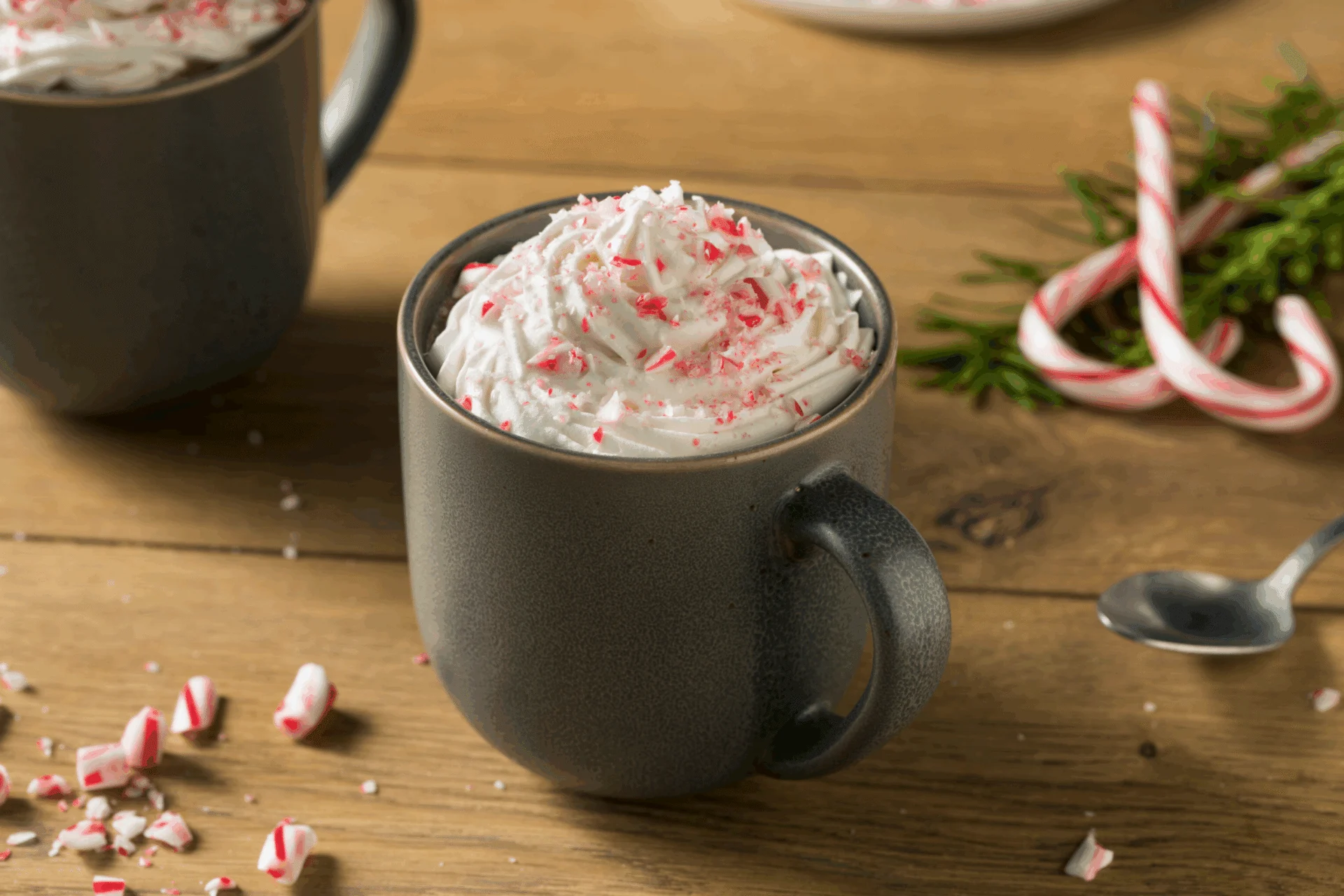 Mug of hot chocolate topped with whipped cream and crushed peppermint, with candy canes on a wooden table