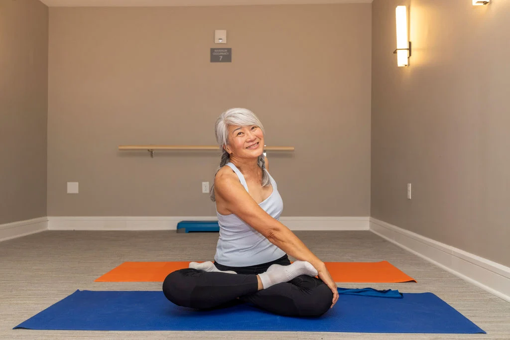 Smiling older woman sitting cross-legged on a yoga mat in an exercise studio