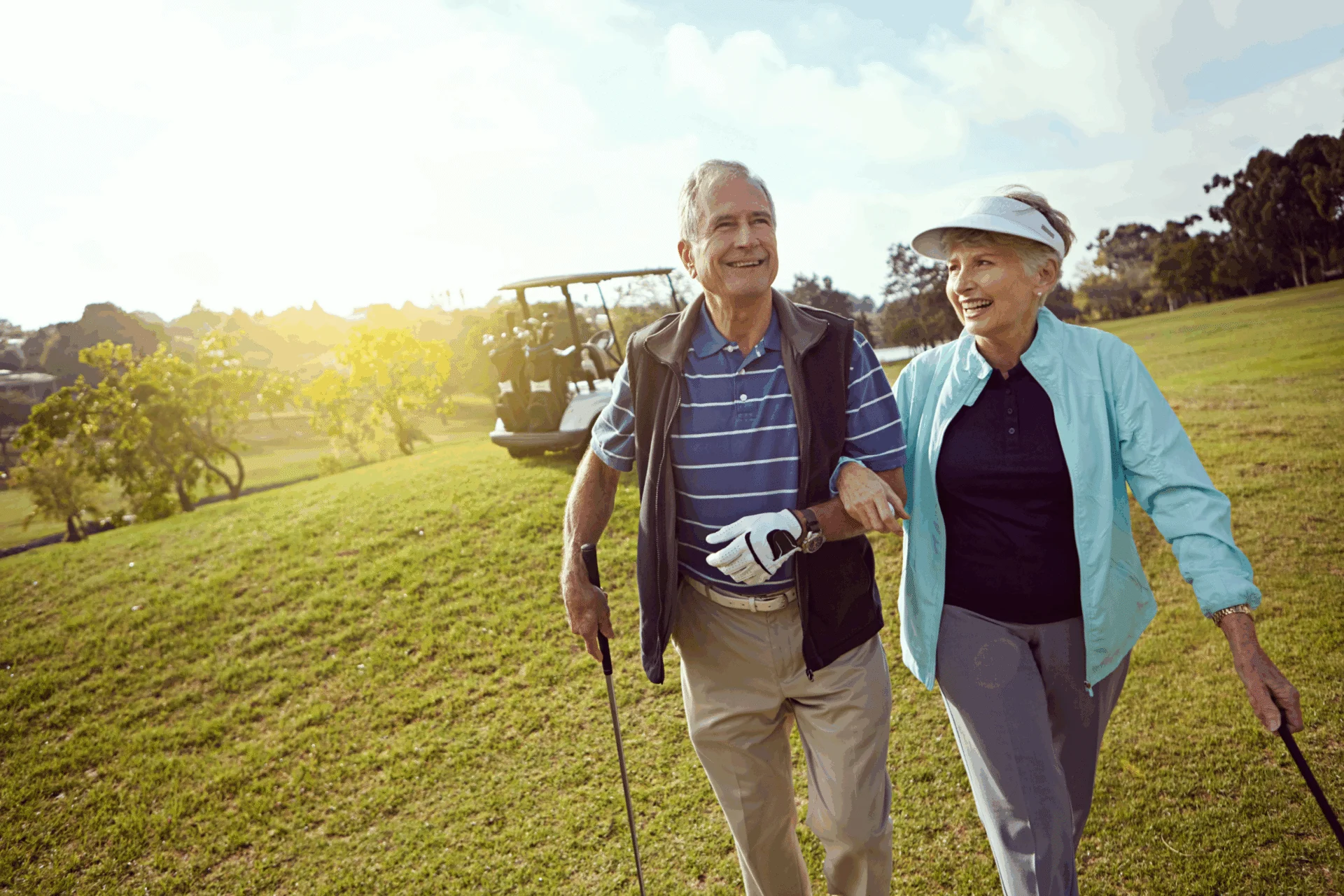 Smiling older couple walking arm in arm across a golf course with golf clubs