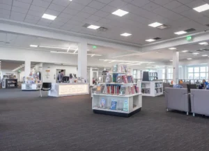 Library interior with bookshelves and displays and lounge chairs, under a ceiling with recessed lights
