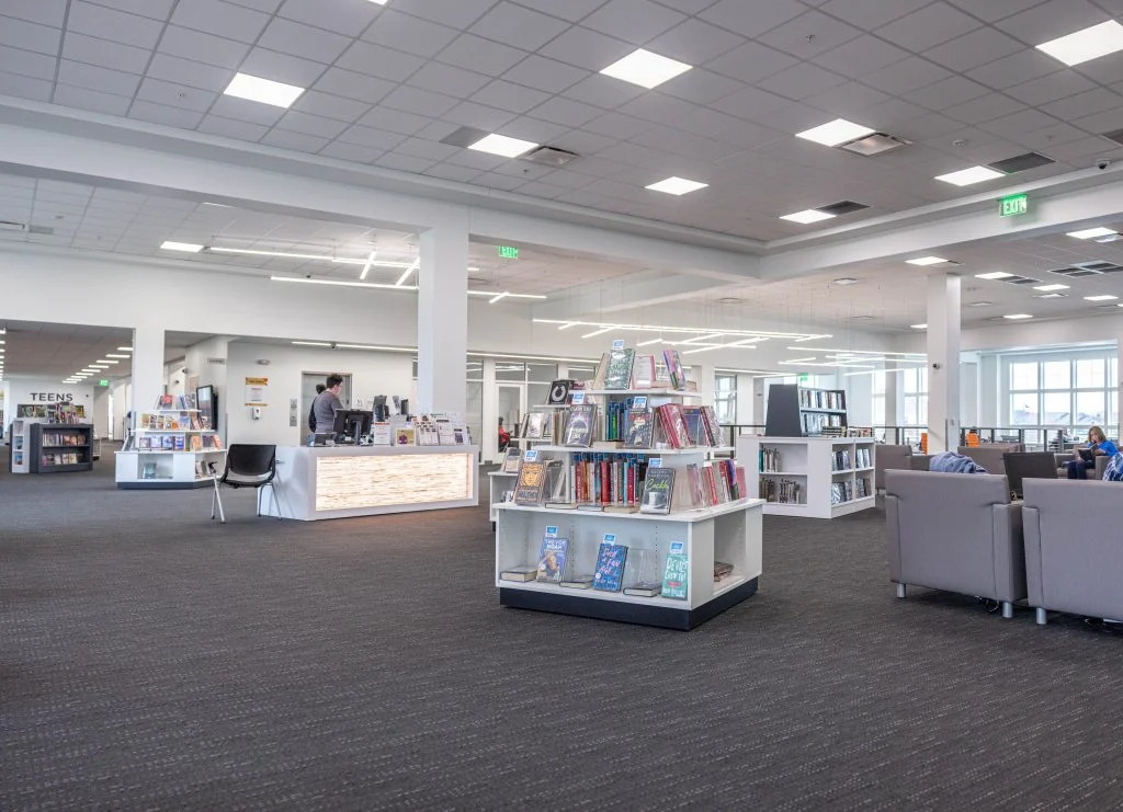 Library interior with bookshelves and displays and lounge chairs, under a ceiling with recessed lights