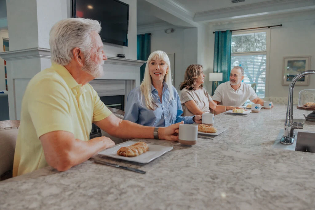 Older adults chatting and eating pastries at a kitchen island