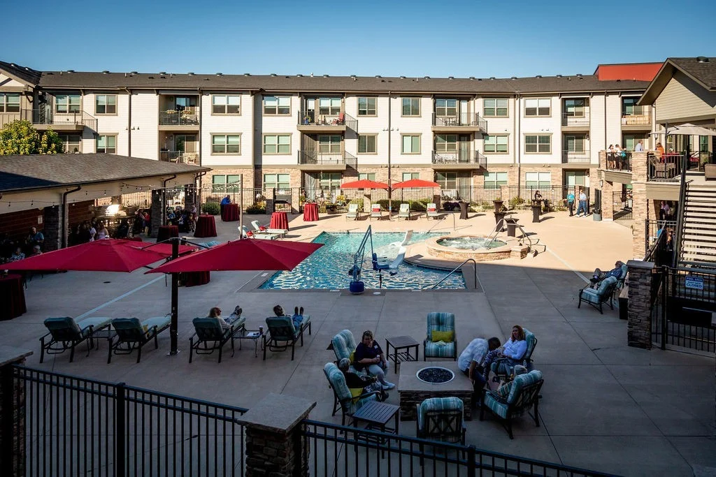 Courtyard with a pool, patio seating and red umbrellas surrounded by a multi-story apartment building