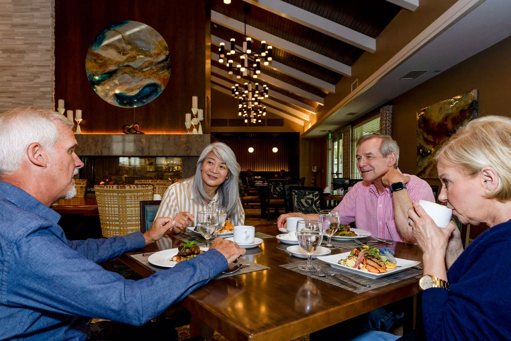 Group of older adults sharing a meal at a wooden table in a warmly lit restaurant
