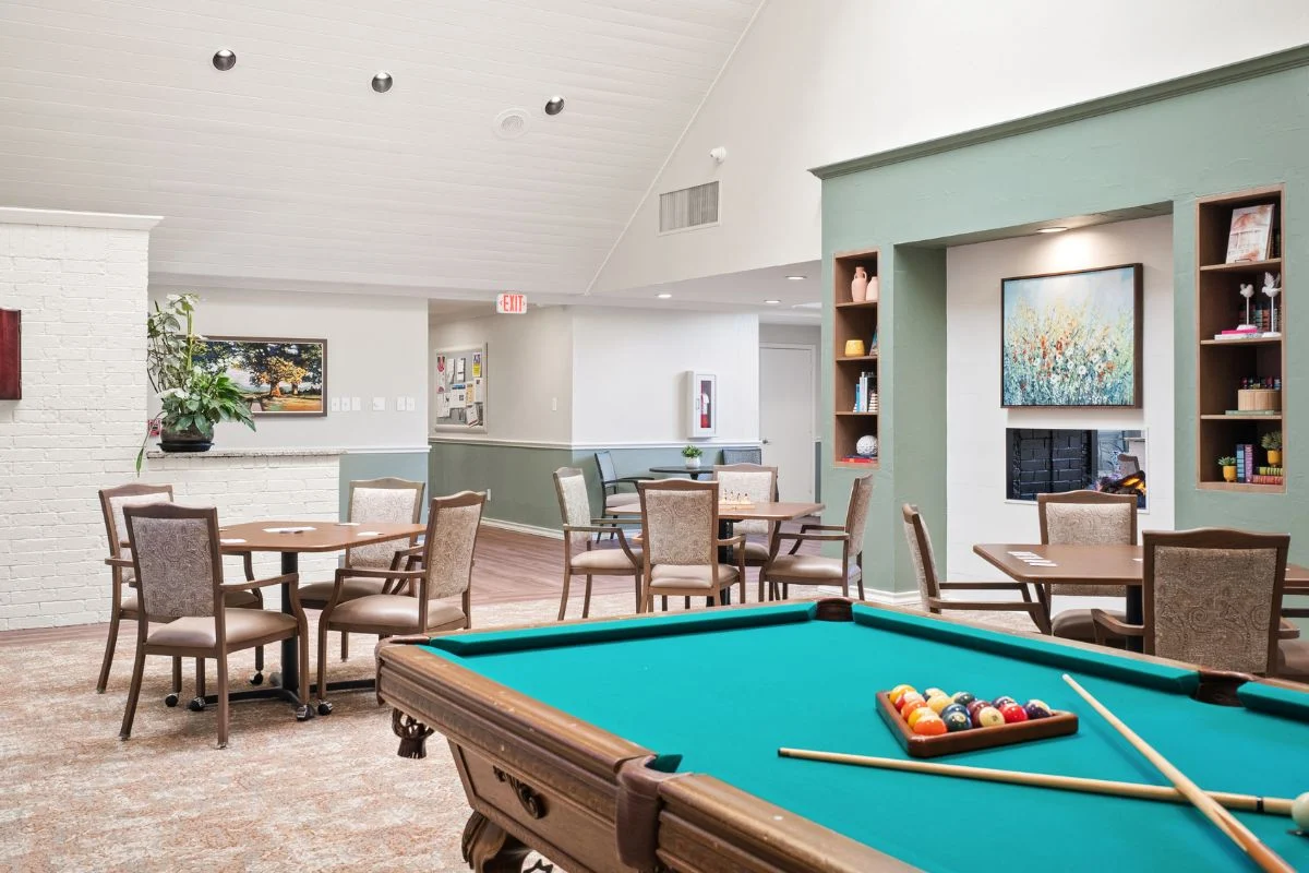 Game room with a teal pool table set up with balls, tables and chairs, and built-in shelves