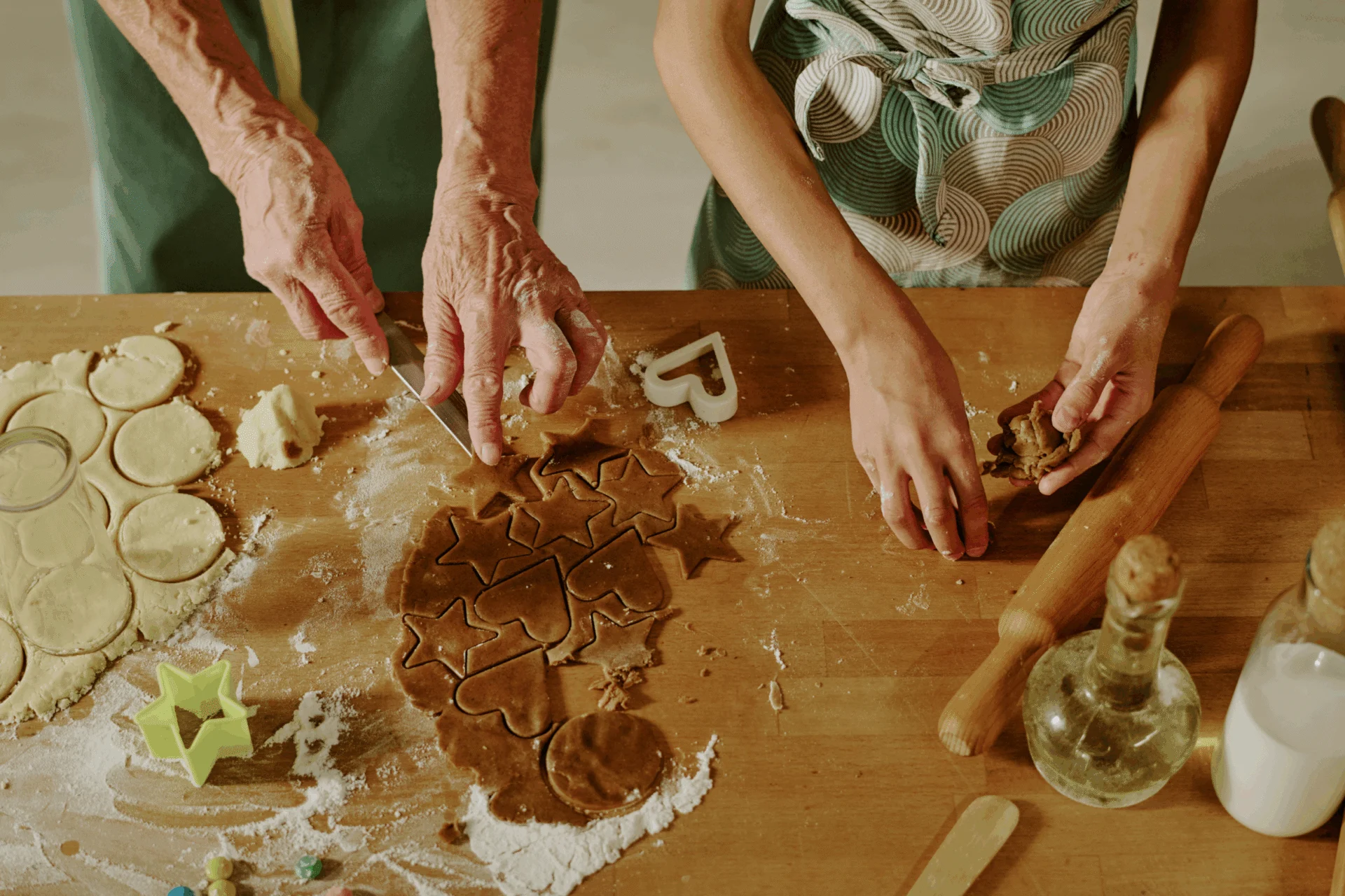 Overhead view of hands cutting shapes out of rolled cookie dough on a wooden board