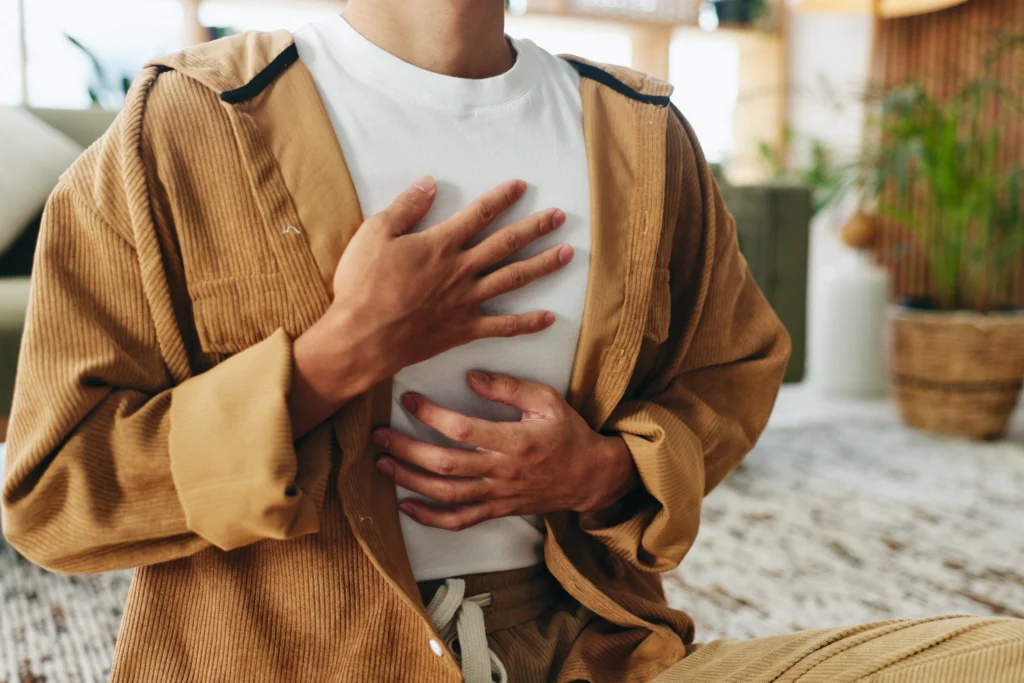 Person in a tan jacket with both hands resting on their chest