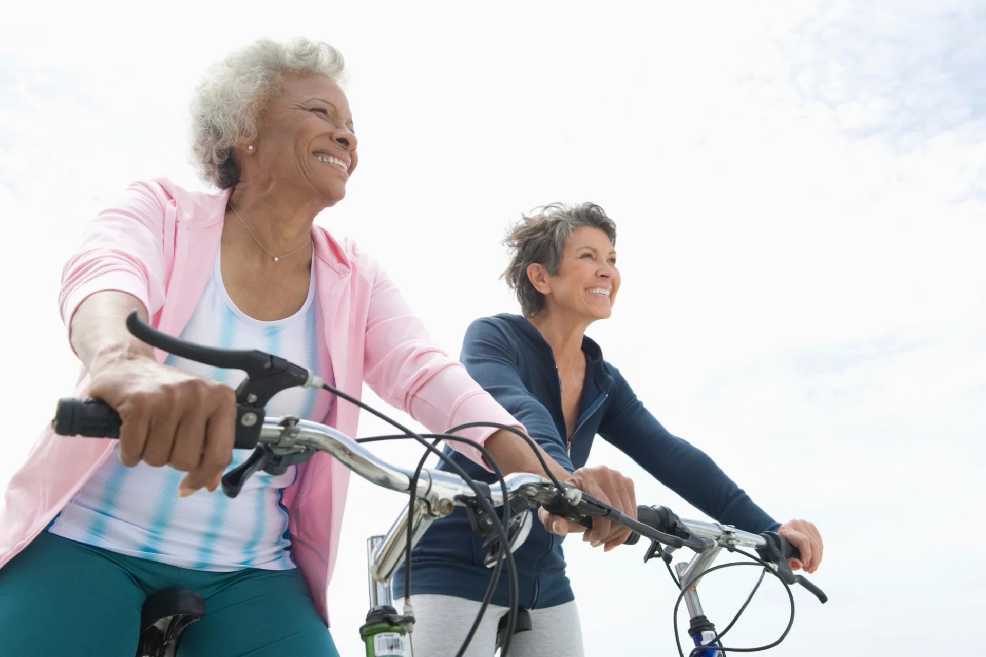 Two smiling older women riding bicycles outdoors