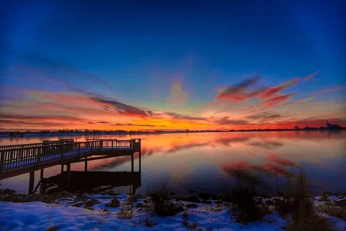 Sunset over a calm lake with a wooden dock and a vivid orange and purple sky