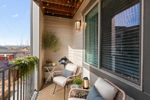 Balcony with cushioned chairs, a lantern and hanging plants beside a shuttered window