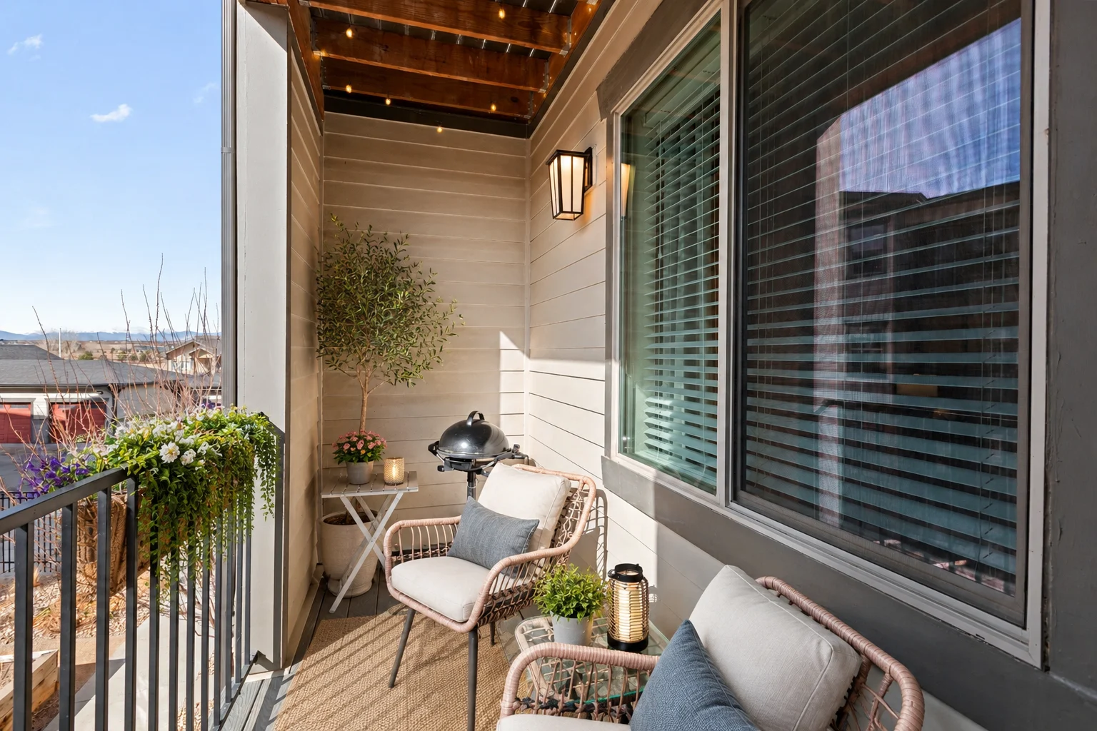 Balcony with cushioned chairs, a lantern and hanging plants beside a shuttered window