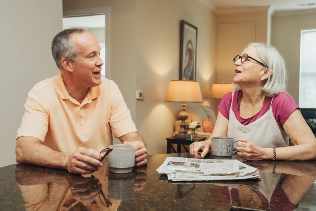 Older man and woman smiling over coffee and a newspaper at a table
