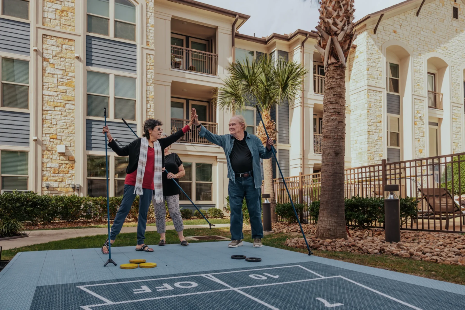 Residents playing shuffleboard on an outdoor court beside a palm-lined apartment building