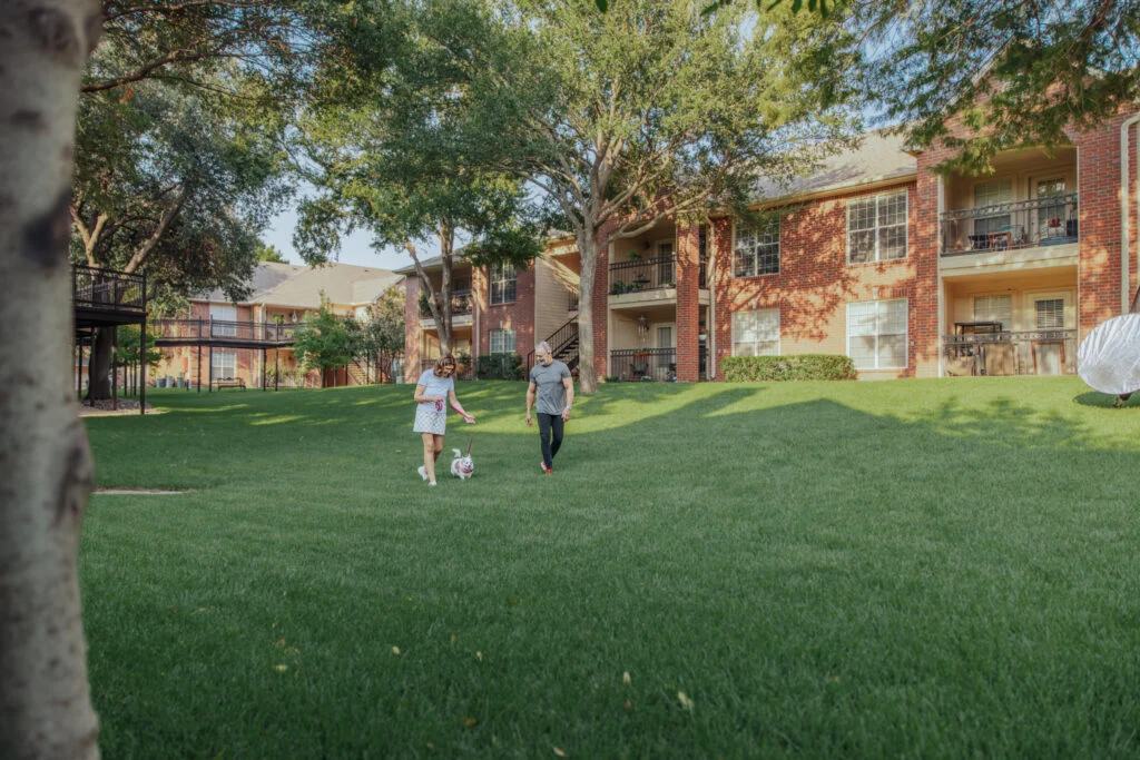 Two people walking across a lawn in front of a brick apartment building