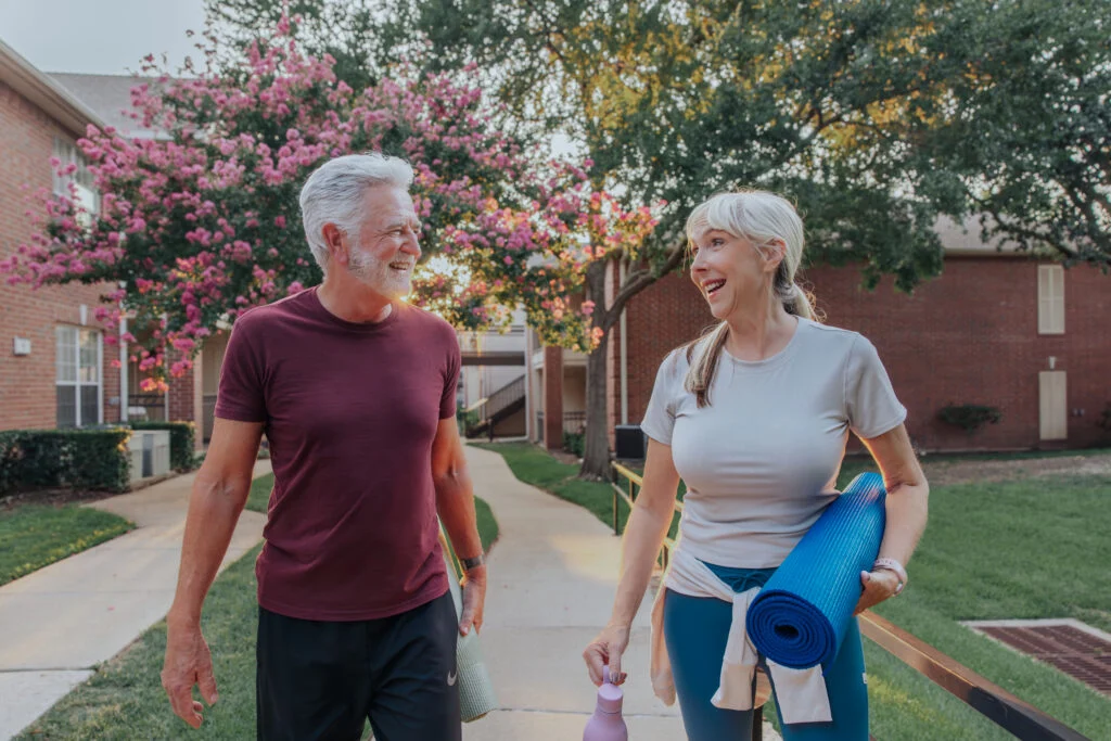 Smiling older couple walking on a path, the woman carrying a rolled-up yoga mat