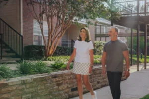 Couple walking along a paved path beside a low stone wall and shrubs