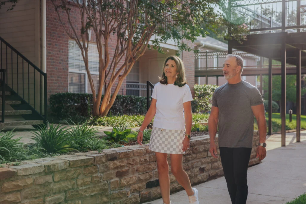 Couple walking along a paved path beside a low stone wall and shrubs
