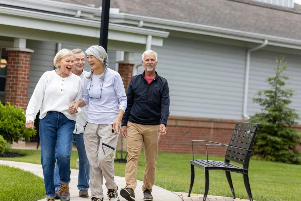 Group of four older adults walking together arm in arm along a sidewalk