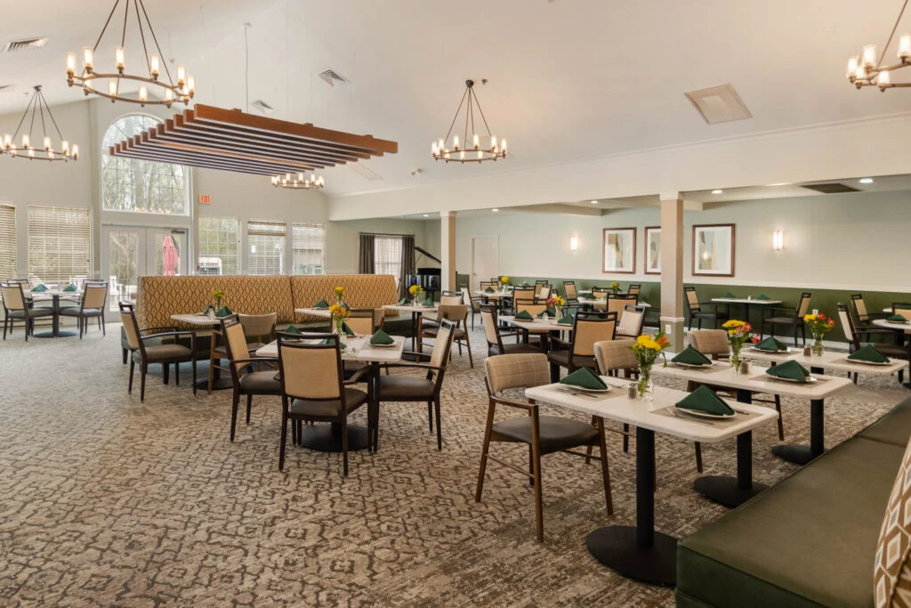 Spacious dining room with square tables set with green place settings, chandeliers and a beamed ceiling