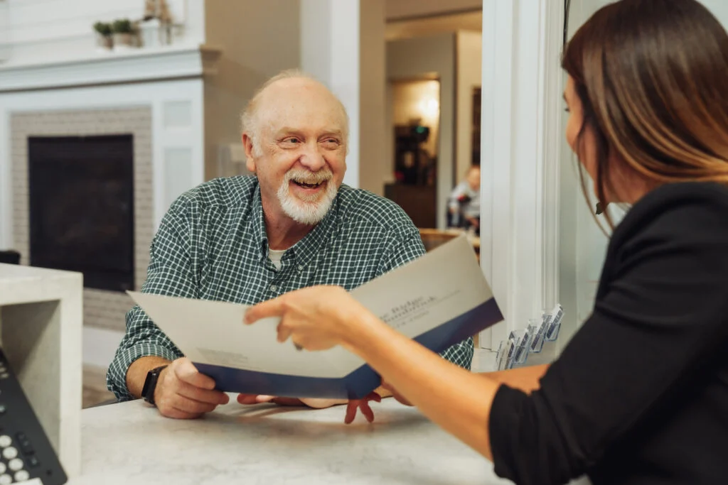 Smiling older man reviewing a brochure with a woman in a black blazer