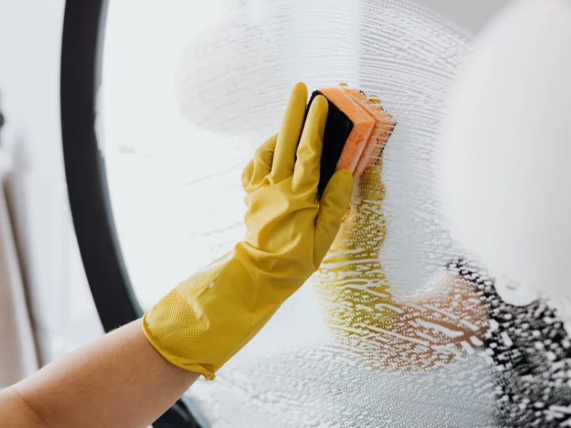 Yellow-gloved hand scrubbing a mirror with a sponge