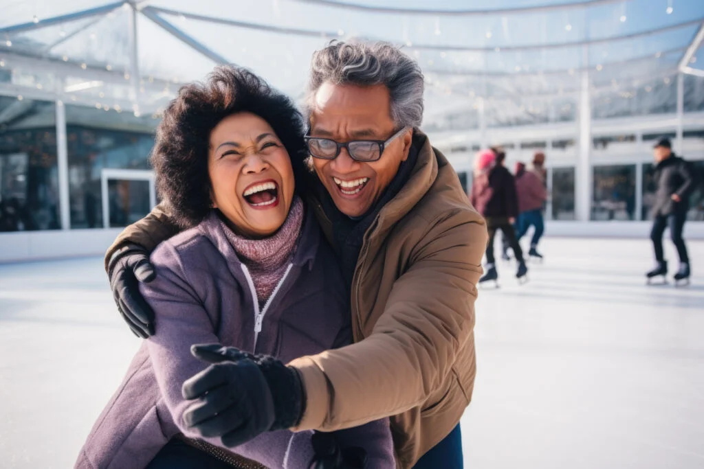 Laughing older couple in winter coats embracing on an ice rink, with skaters behind them