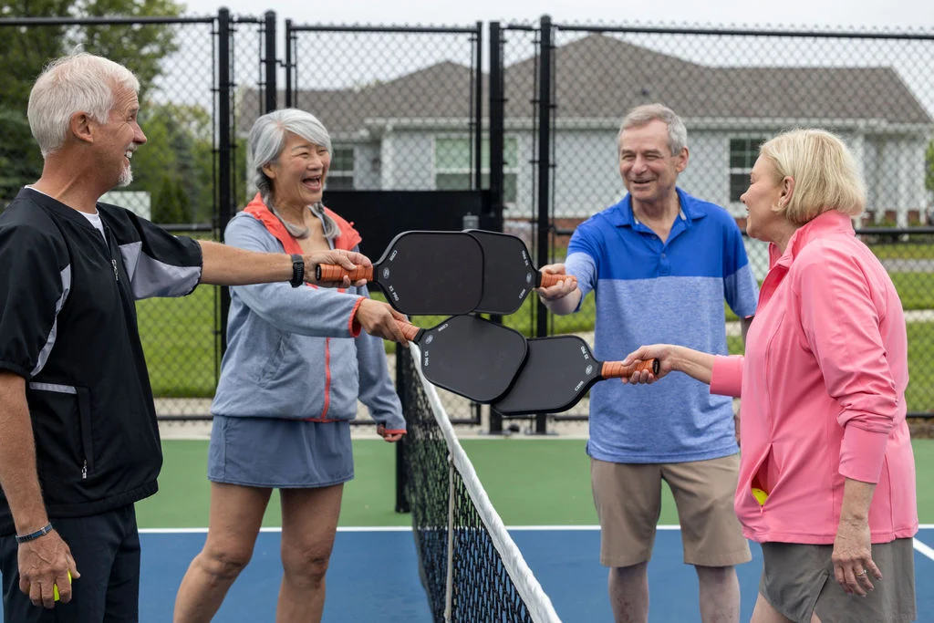 Four older adults chatting and shaking hands at a pickleball court net